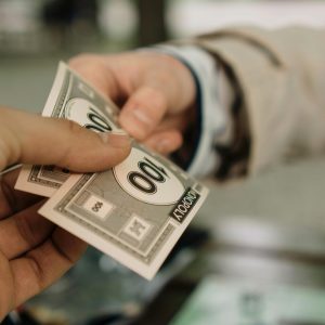 Close-up of two hands exchanging Monopoly money, symbolizing a financial transaction.